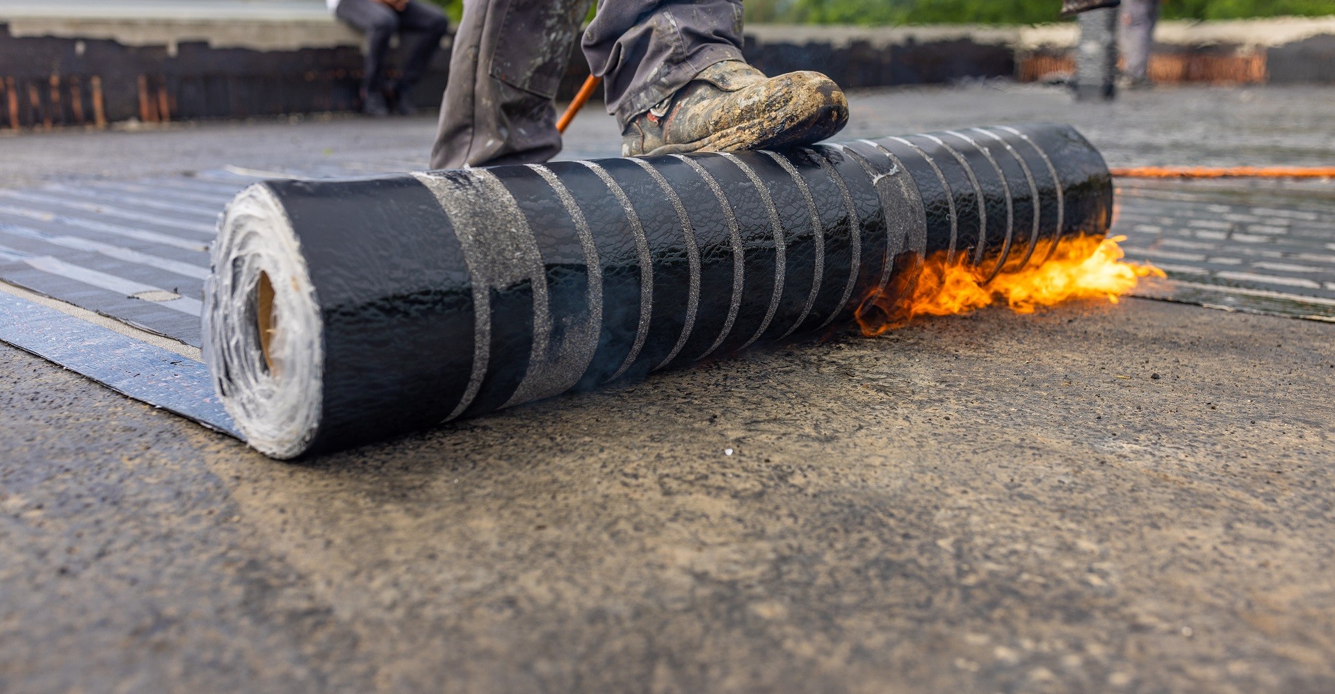 Workers placing a vapor barrier on the roof using a propane gas torch for welding bitumen sheets.
